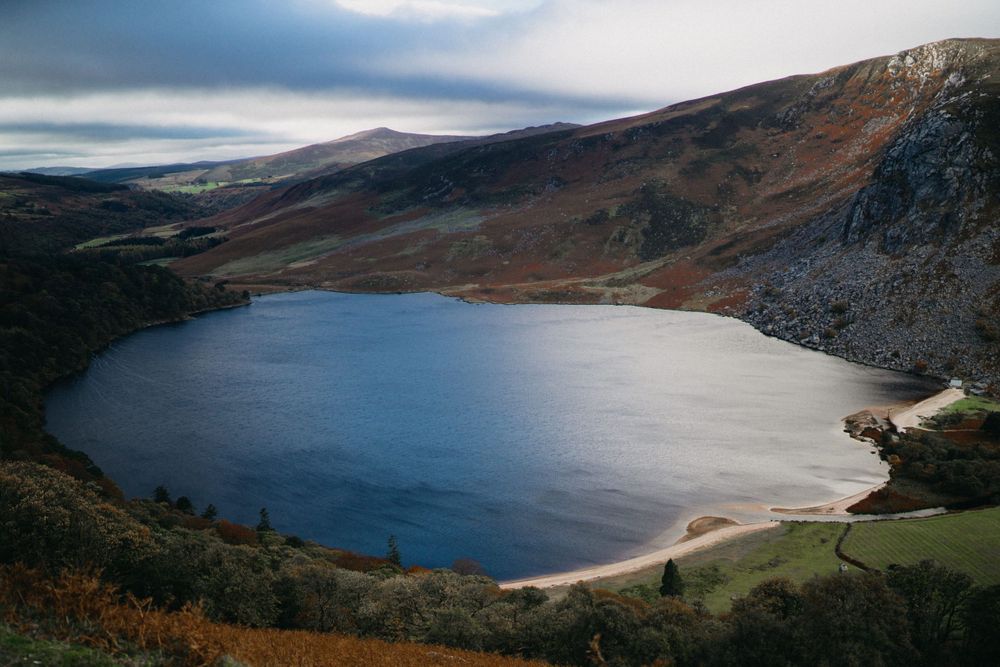 Scenic mountain reservoir surrounded by rolling hills and dramatic cloudy skies.