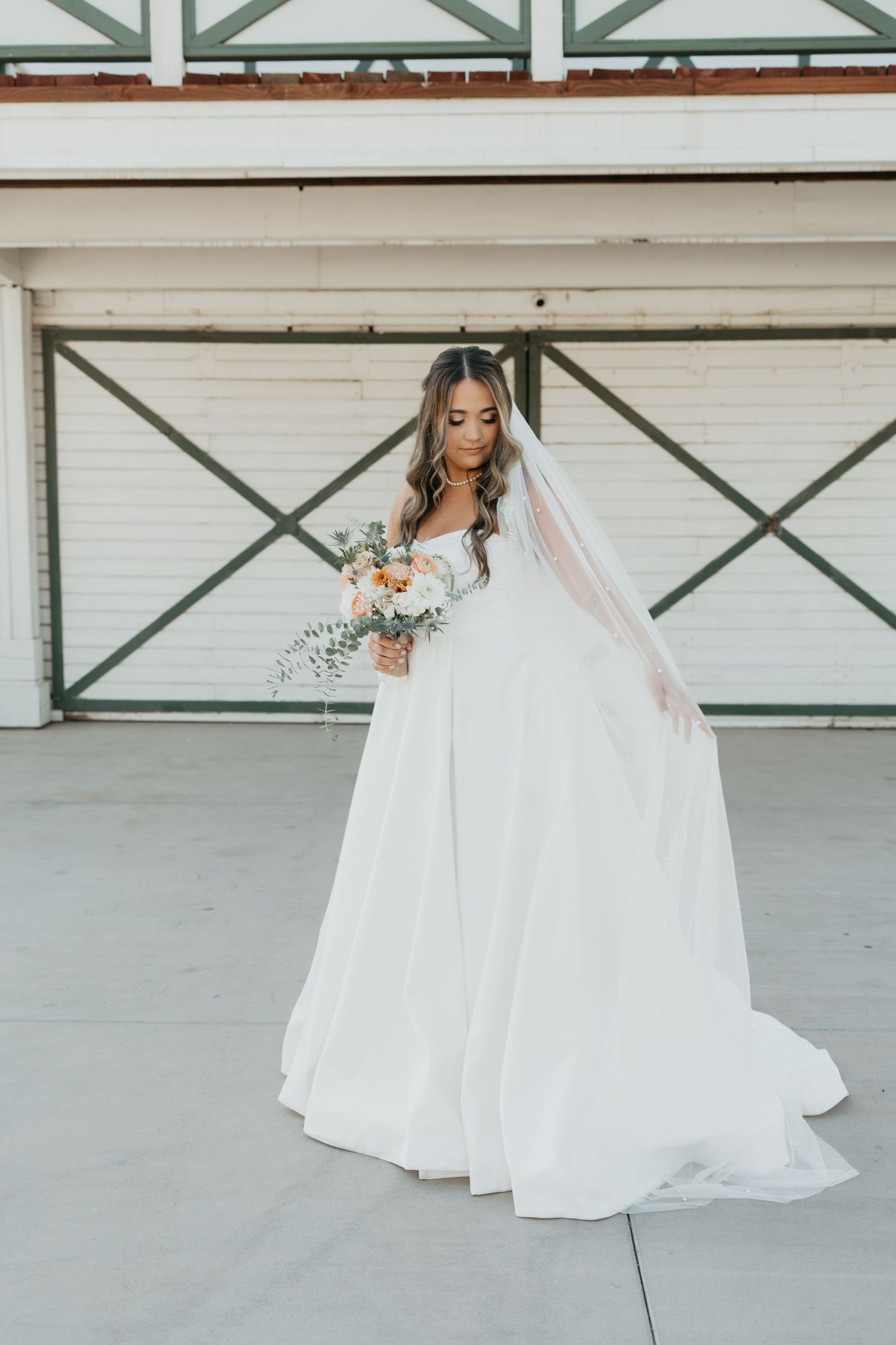 A radiant bride poses in an elegant white gown with flowing veil and holds a soft pastel bouquet.