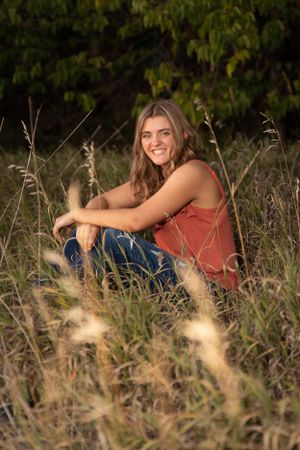 becky katzberg photography senior girl sitting in tall grass in a coral shirt