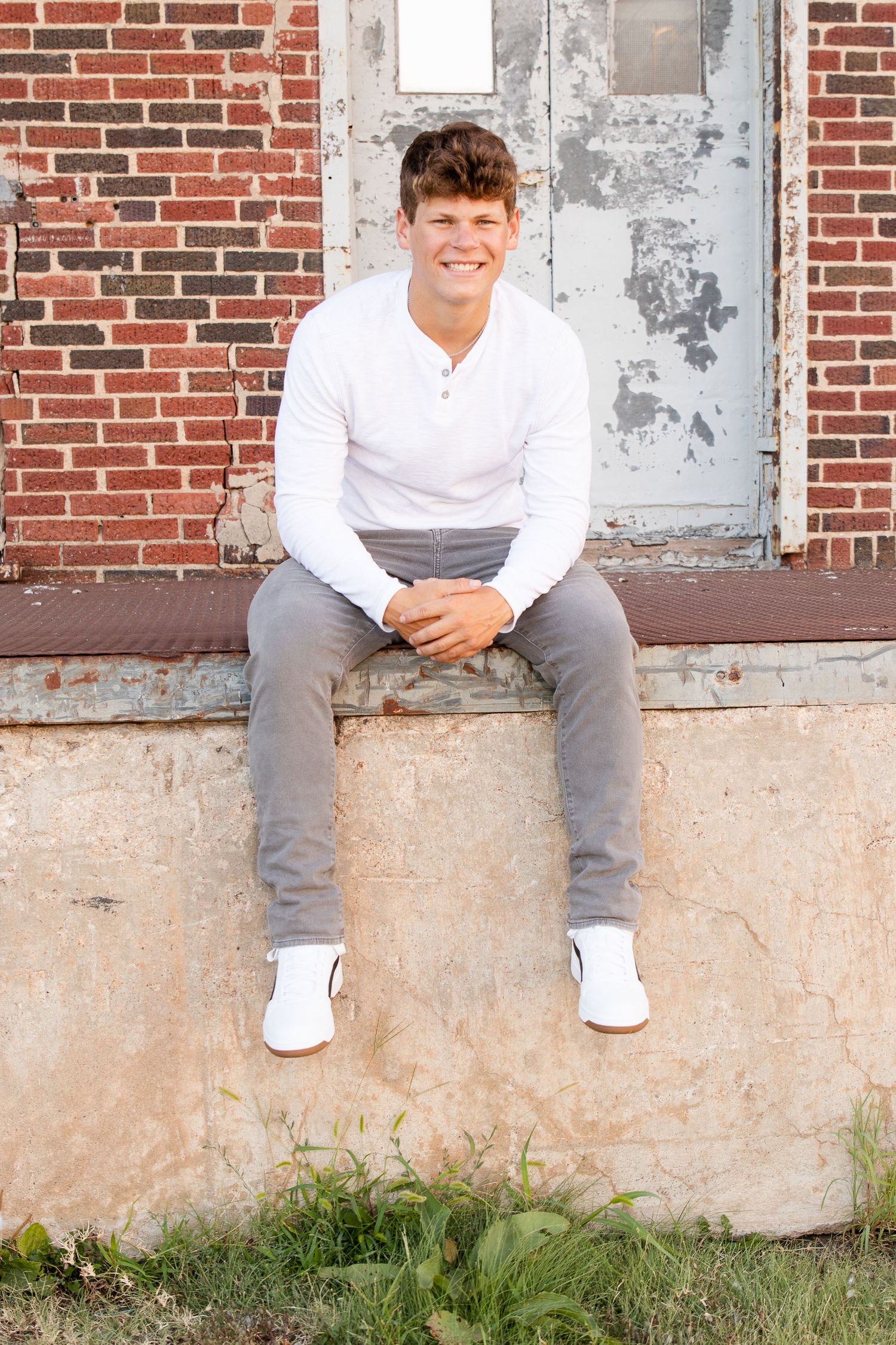 becky katzberg photography senior boy with white shirt and gray pants sitting on a loading dock