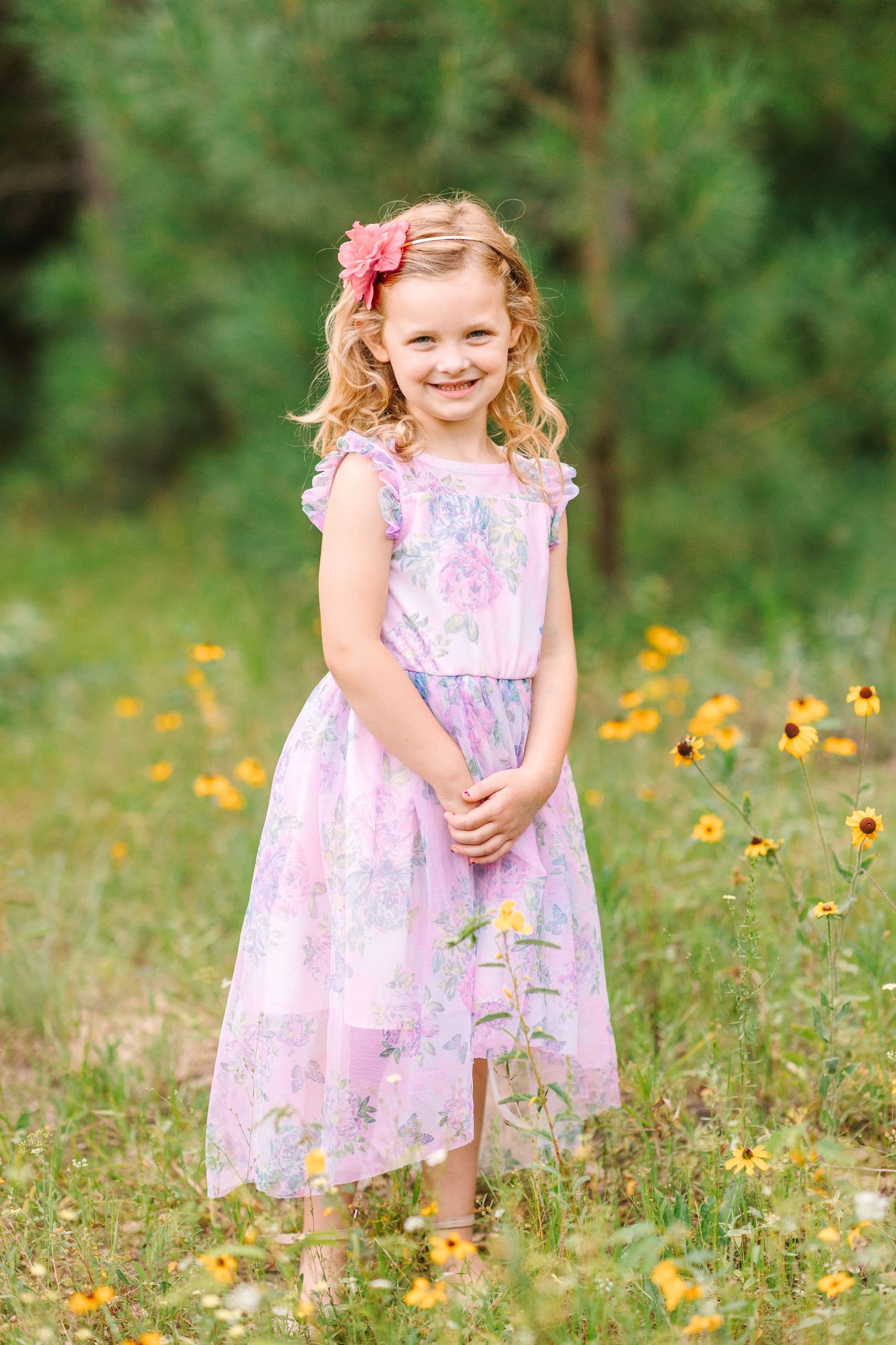 Young child in purple dress standing among yellow wildflowers.