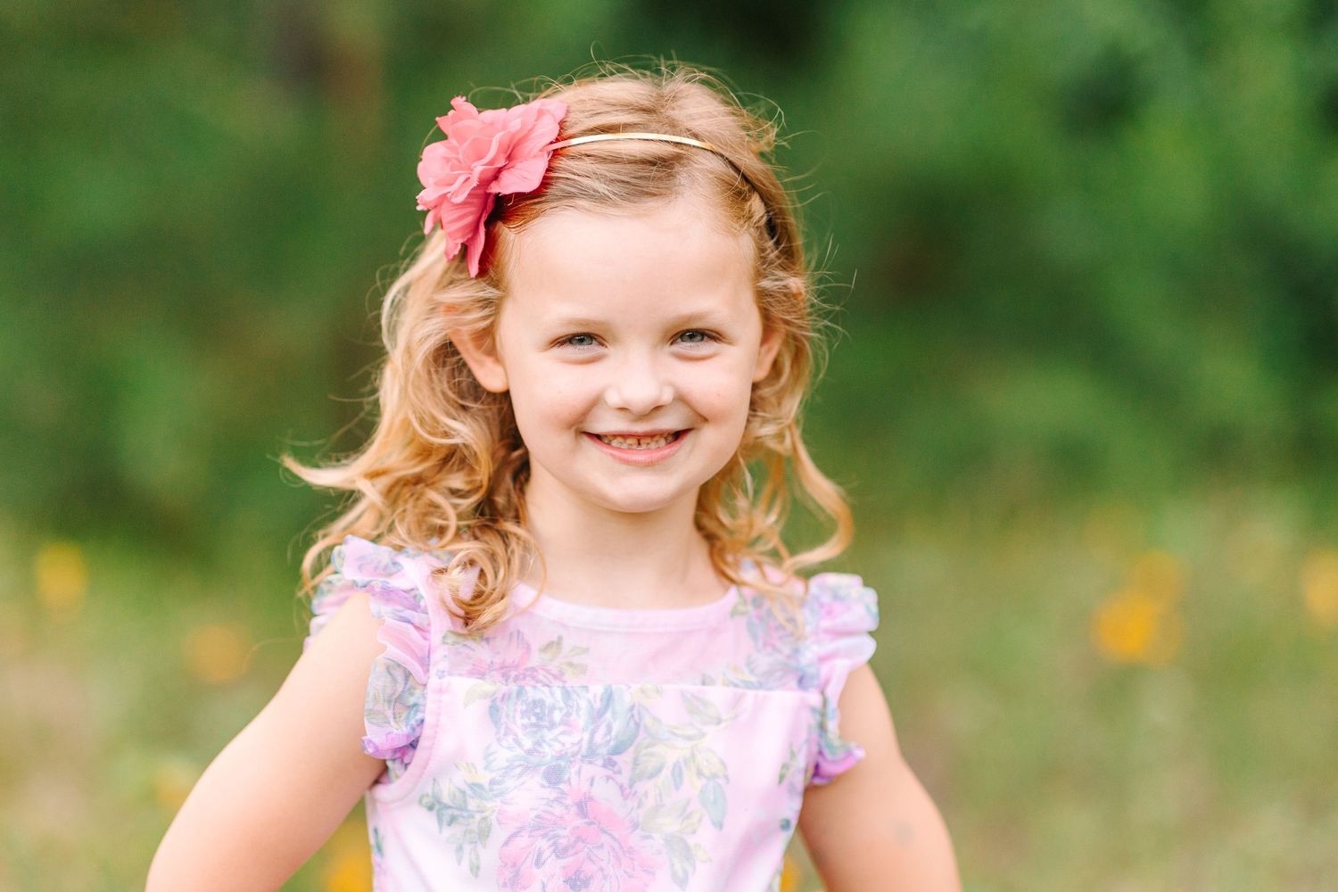 Close up portrait of child wearing purple floral dress and pink hair flower.