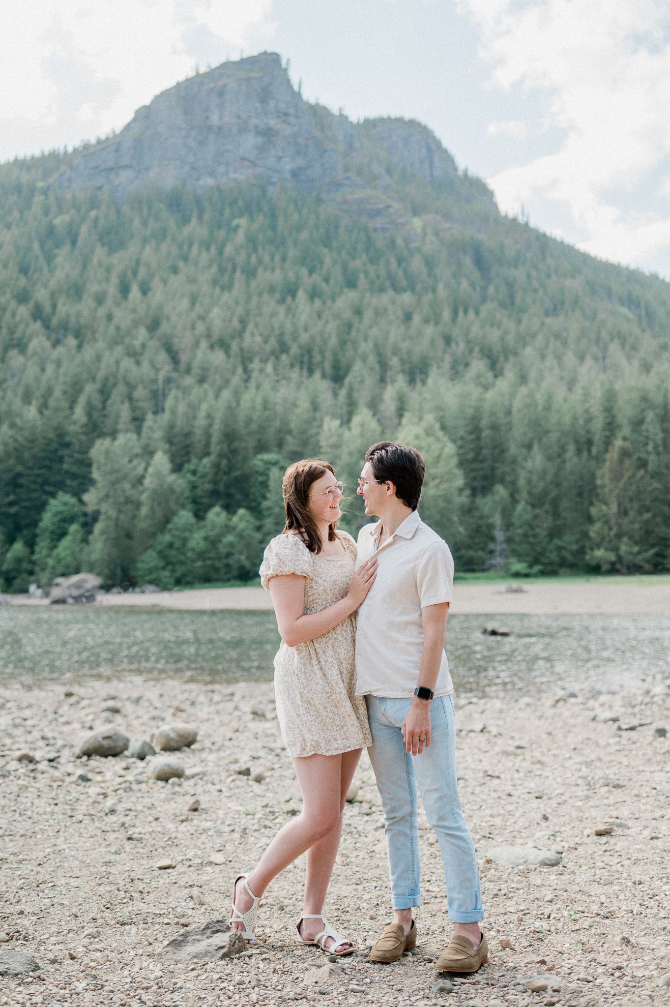 A couple shares a romantic moment on a rocky beach with Rattlesnake Ledge behind them. Photo by Pine + Vow