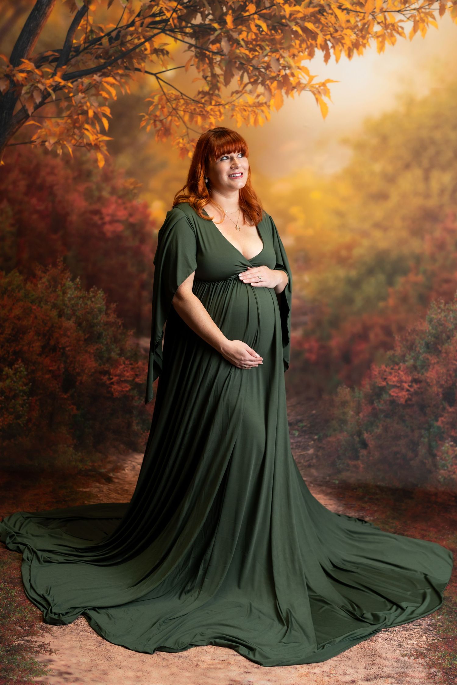 Maternity photoshoot featuring woman in flowing emerald green dress against autumn backdrop.