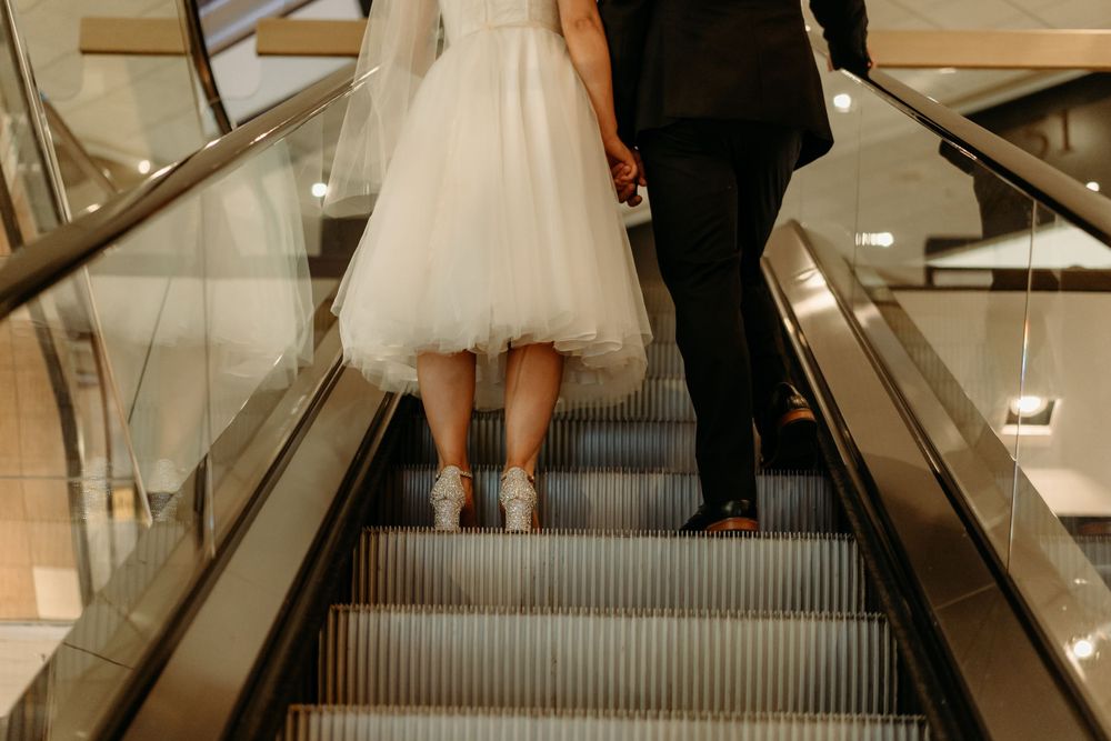 A couple in wedding attire rides an elevator up and hold hands.