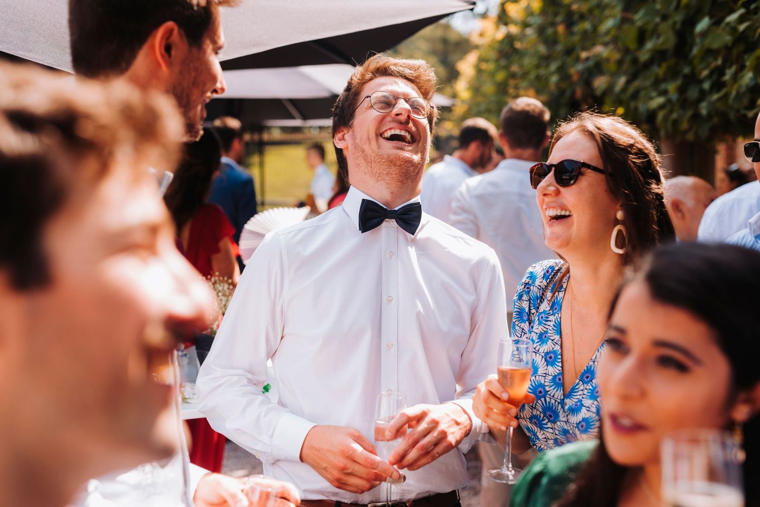 Guests share laughter and champagne during an outdoor wedding reception celebration.
