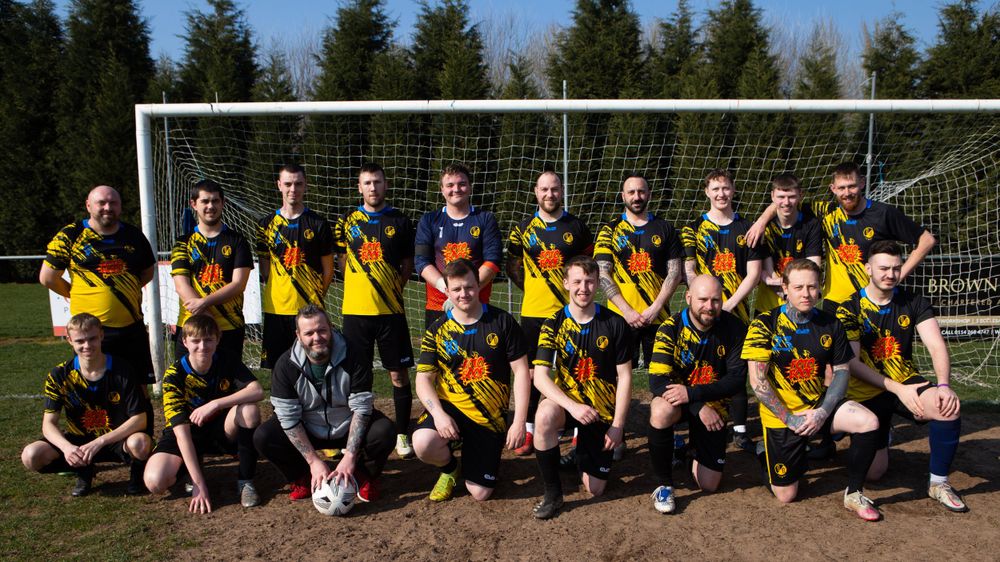Soccer team poses together in front of goal post for team photo.