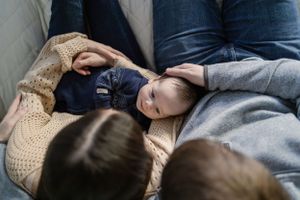 Family shares tender moment together on couch with sleeping infant.