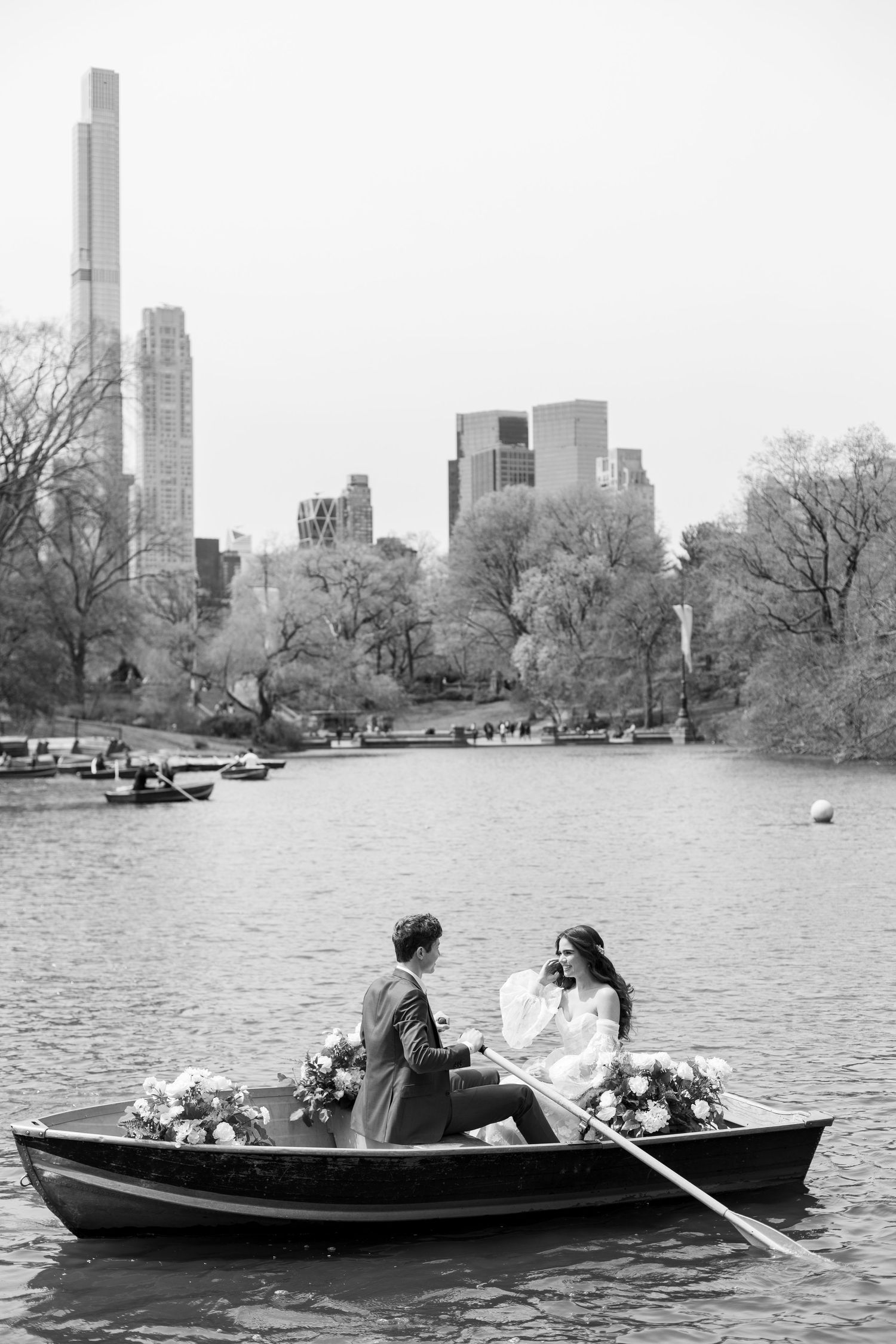 Black and white photo of couple in rowboat with Manhattan skyline backdrop.