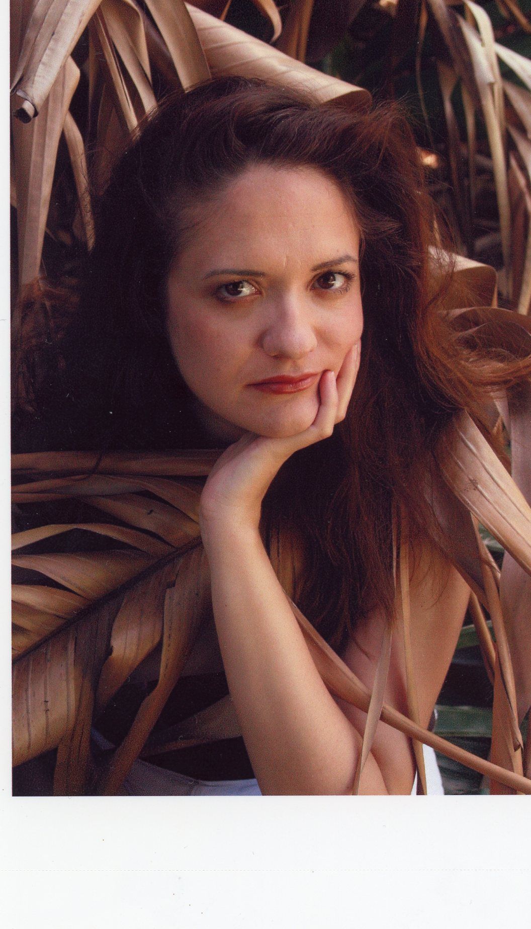 a beautiful young woman posing in front of a palm leaf