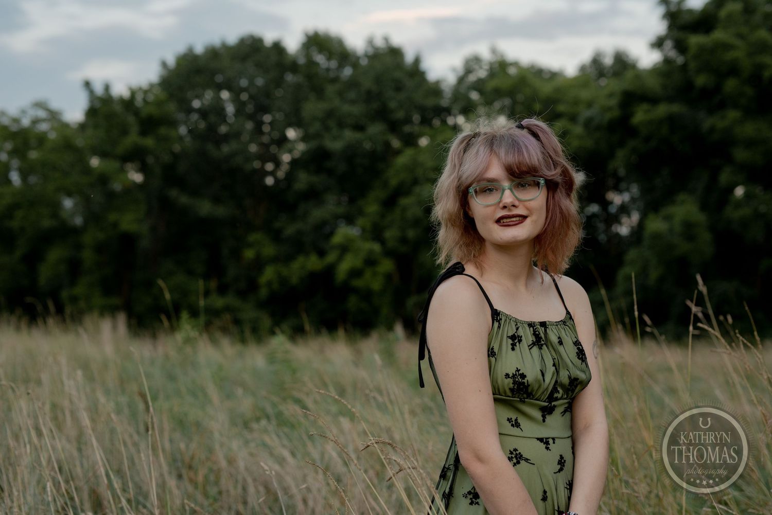 Casual outdoor portrait in a green sundress against a natural field backdrop.