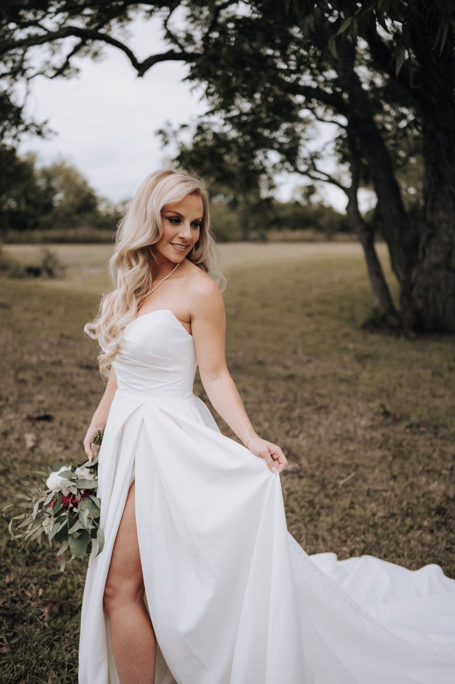 Elegant white wedding dress with flowing skirt and high slit shown against a rustic outdoor backdrop.