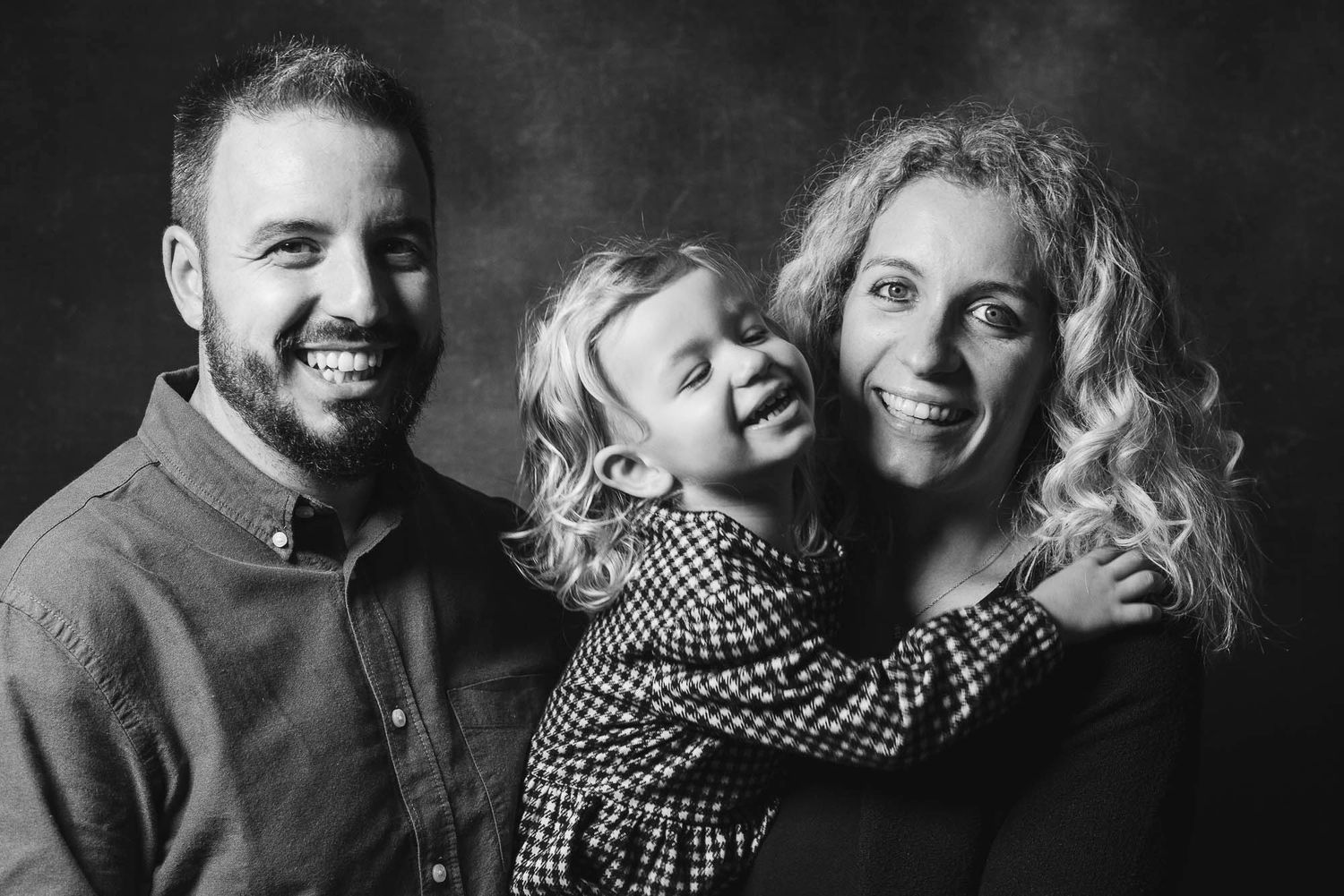 Black and white family portrait showing joyful moment with child between parents.