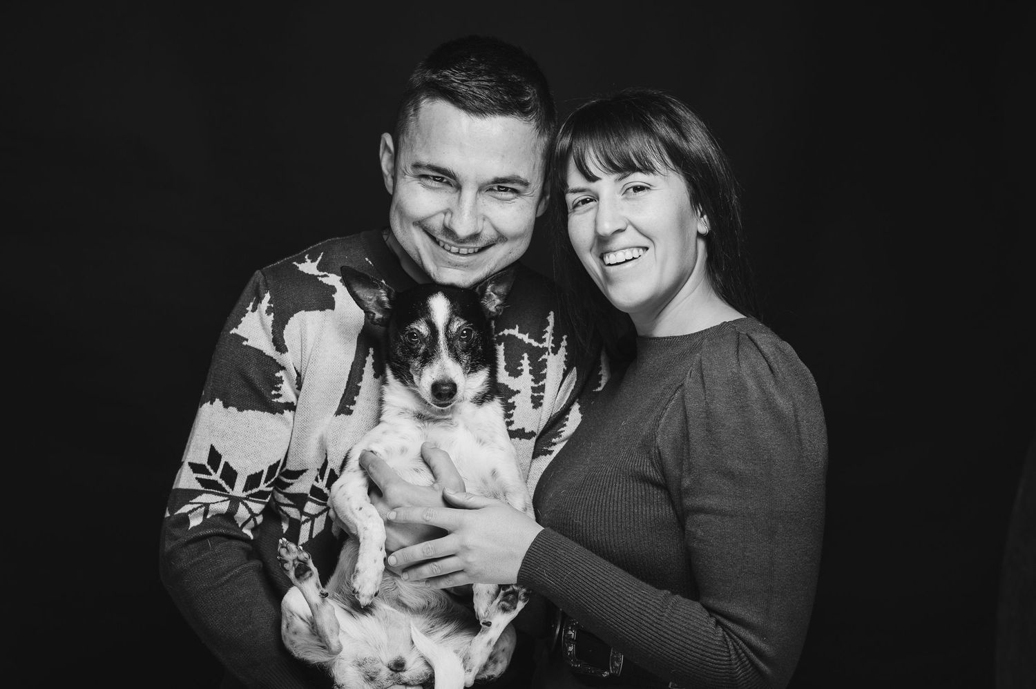 Black and white family portrait featuring a couple holding their small black and white dog.