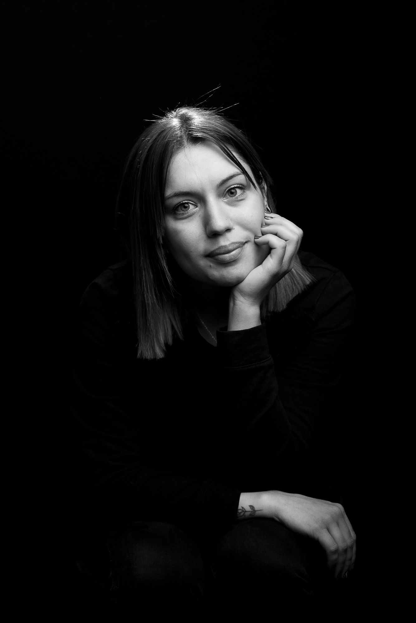 Intimate black and white portrait of person resting chin on hand while gazing at camera.
