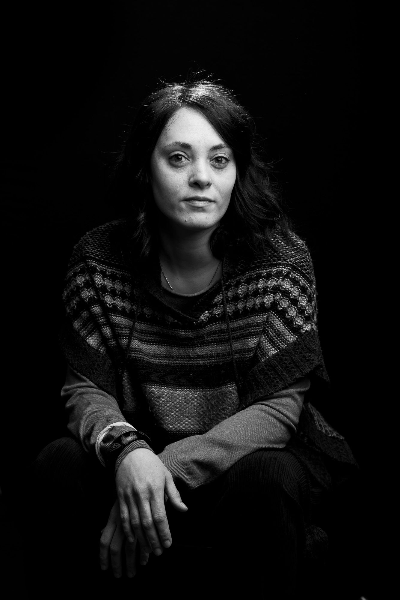 Moody black and white portrait of person wearing striped sweater against dark background.