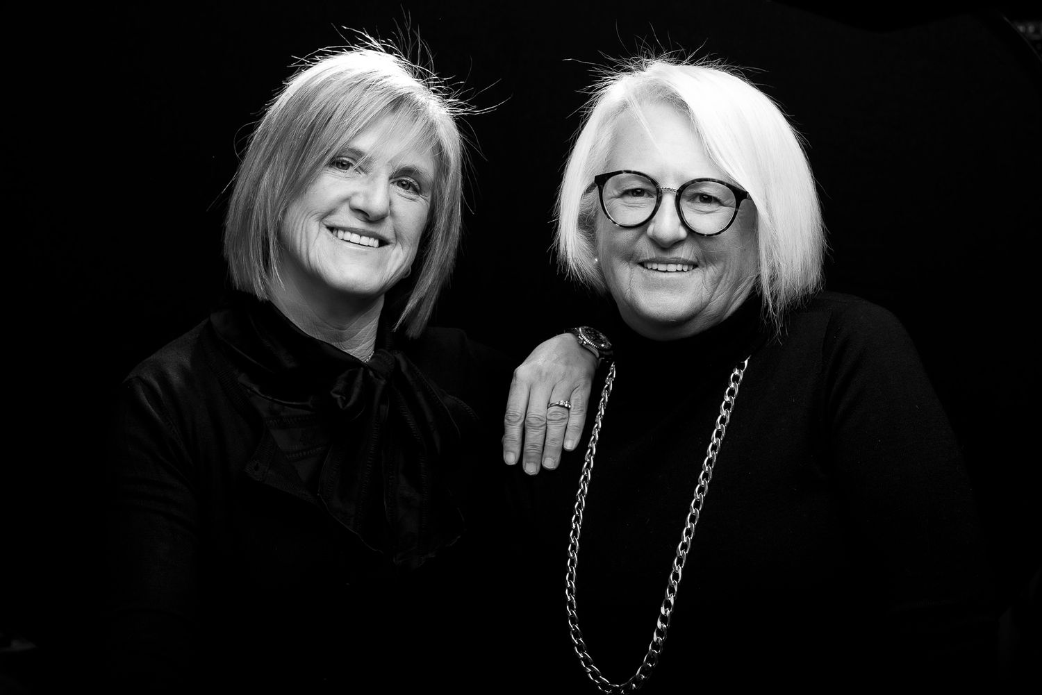 Black and white studio portrait of two people embracing and smiling at camera.