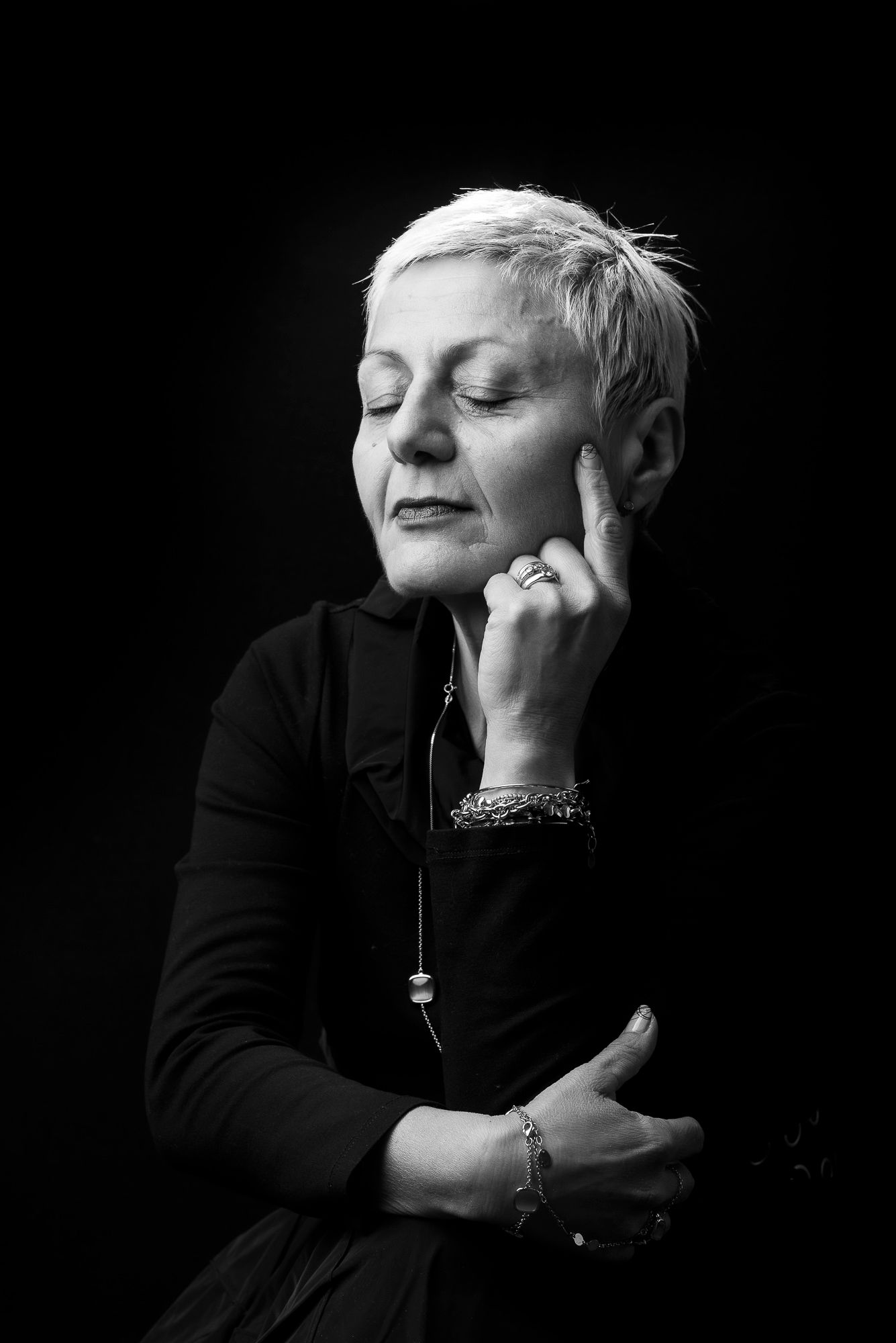 Serene black and white portrait of person with short hair in contemplative pose wearing dark clothing.