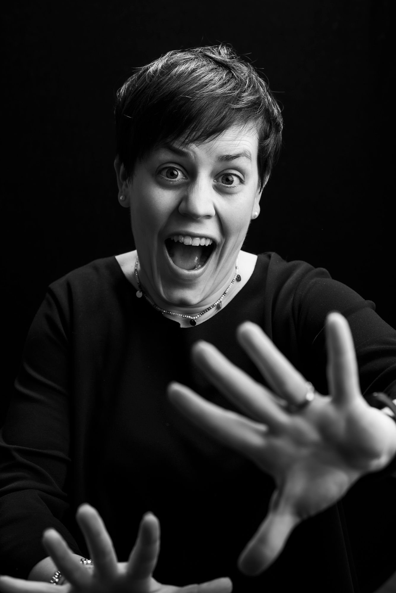 Dramatic black and white portrait showing energetic expression with hands raised against dark background.
