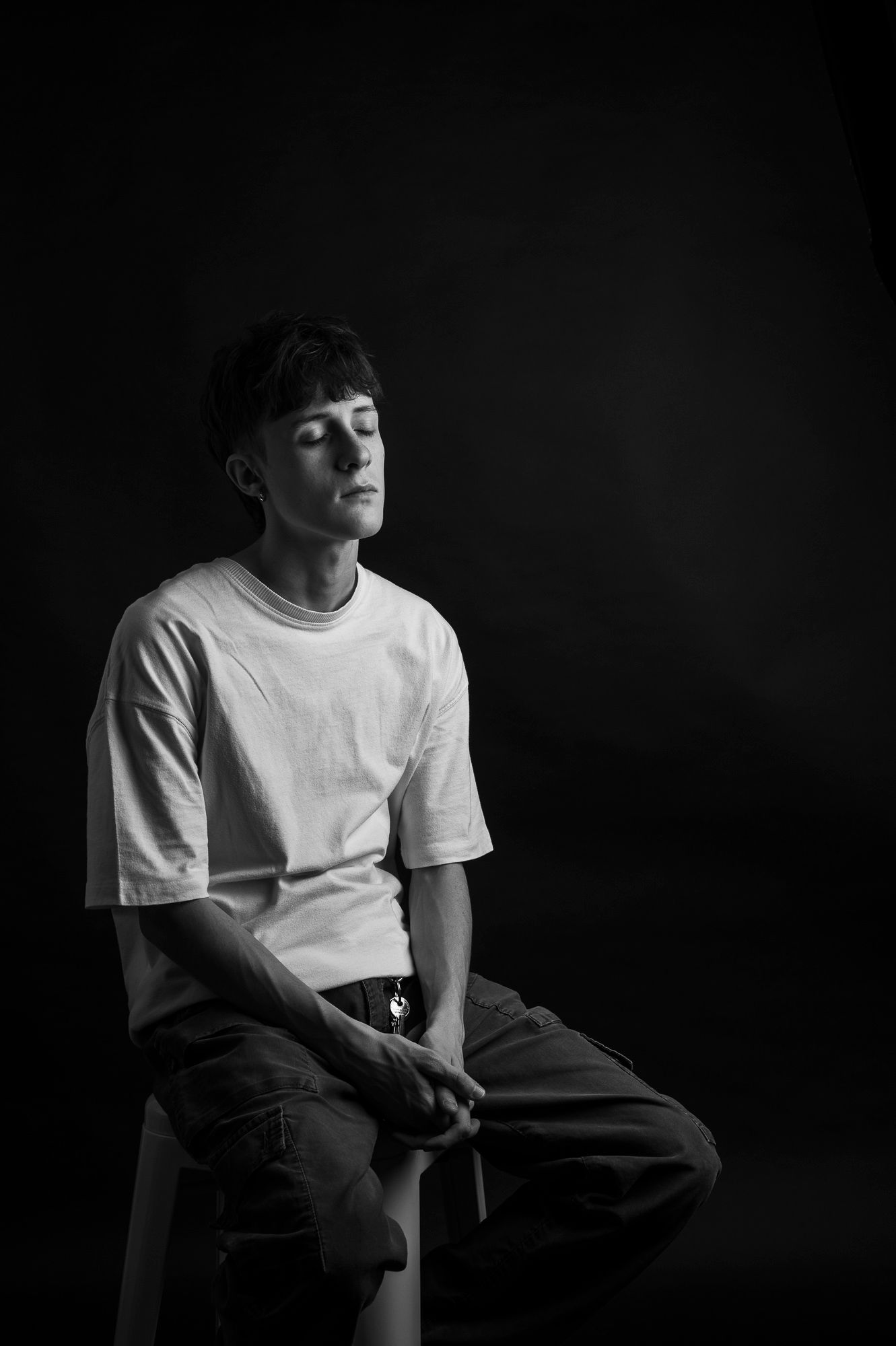 Artistic black and white portrait of a person in a white t-shirt against a dark background.