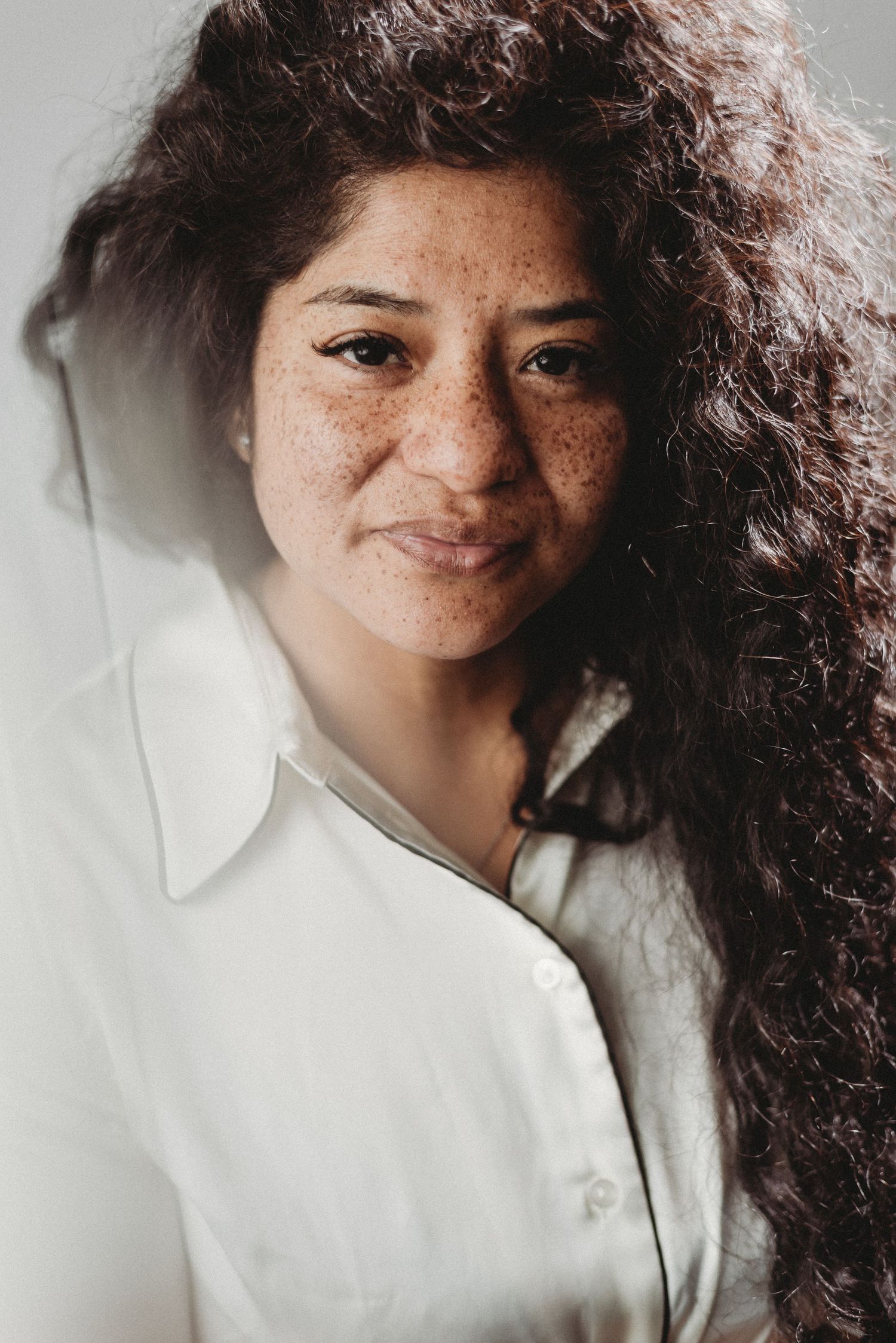 Close-up portrait highlighting natural freckles and curly hair against a light background.