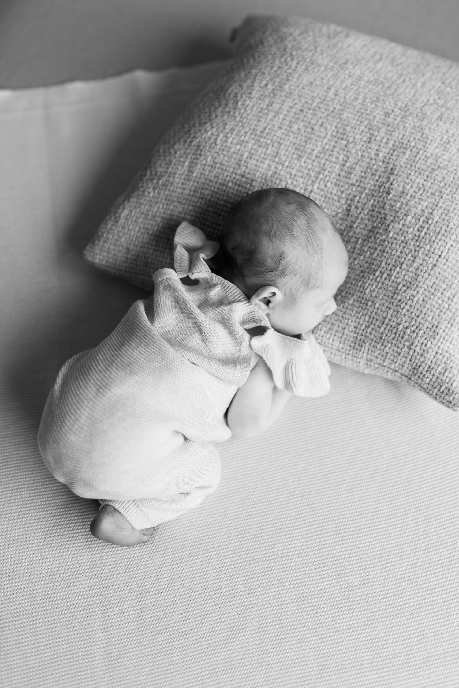 A sleeping newborn wrapped in white lies peacefully on a textured pillow.