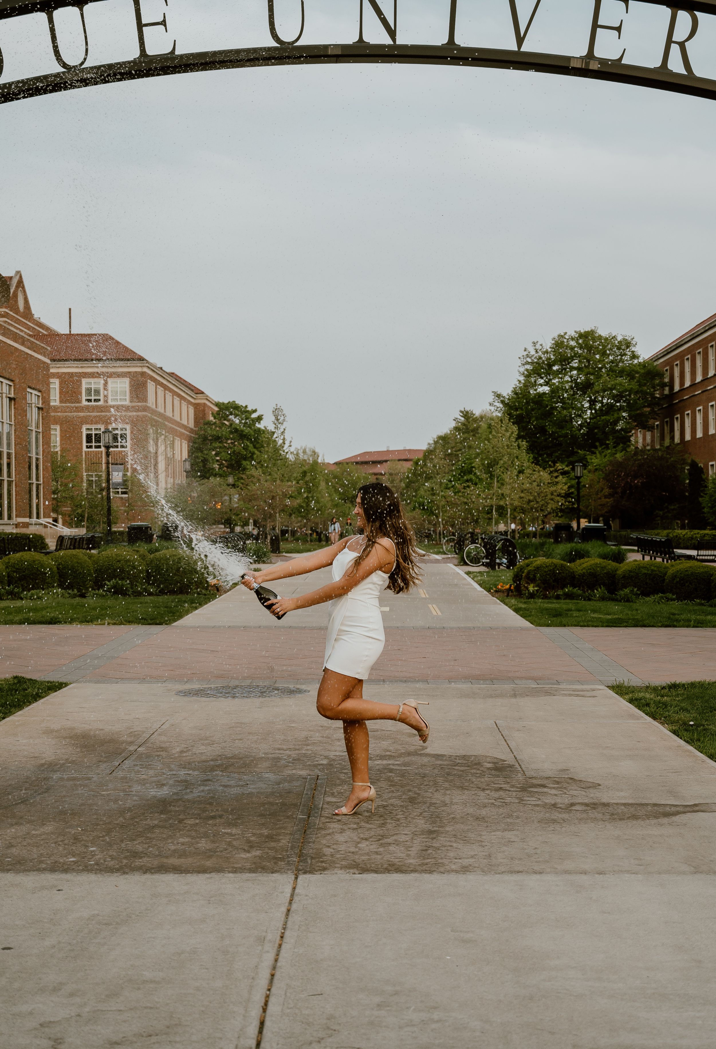Person in white dress twirls joyfully under university entrance arch.