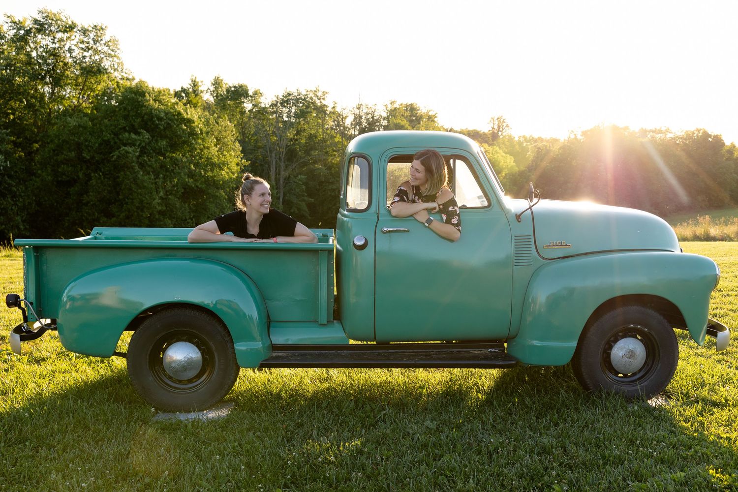 Vintage turquoise pickup truck with dog in countryside at sunset.