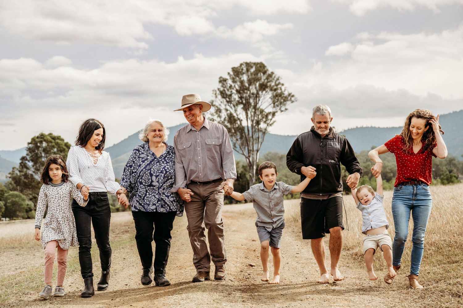 A multigenerational group walking together on a hilltop against a cloudy sky and mountain backdrop.