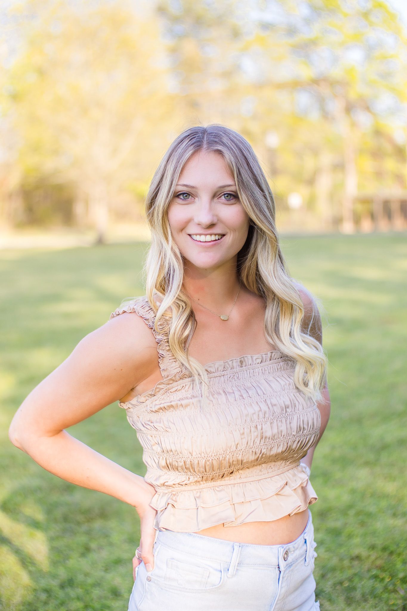 Person in beige smocked top poses outdoors during golden hour with natural lighting.