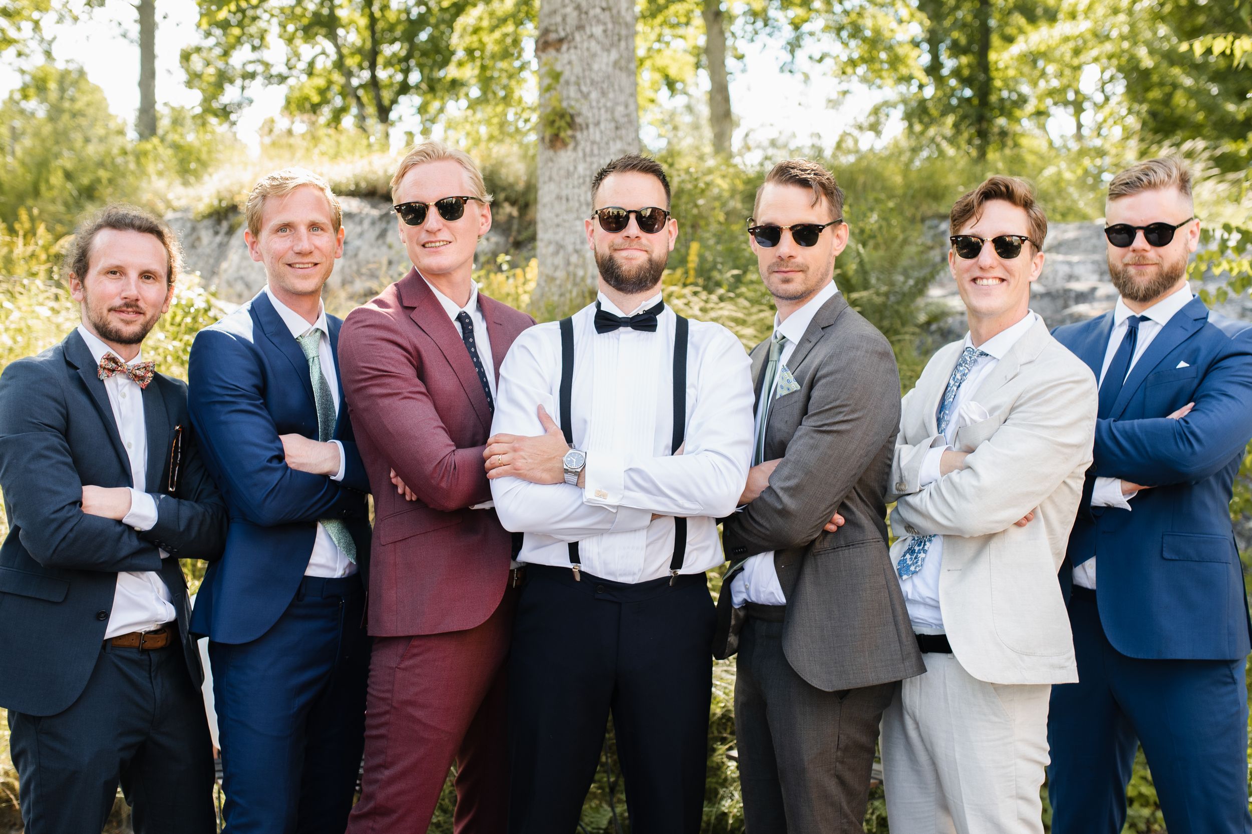Group of wedding party members in colorful suits posing together outdoors.