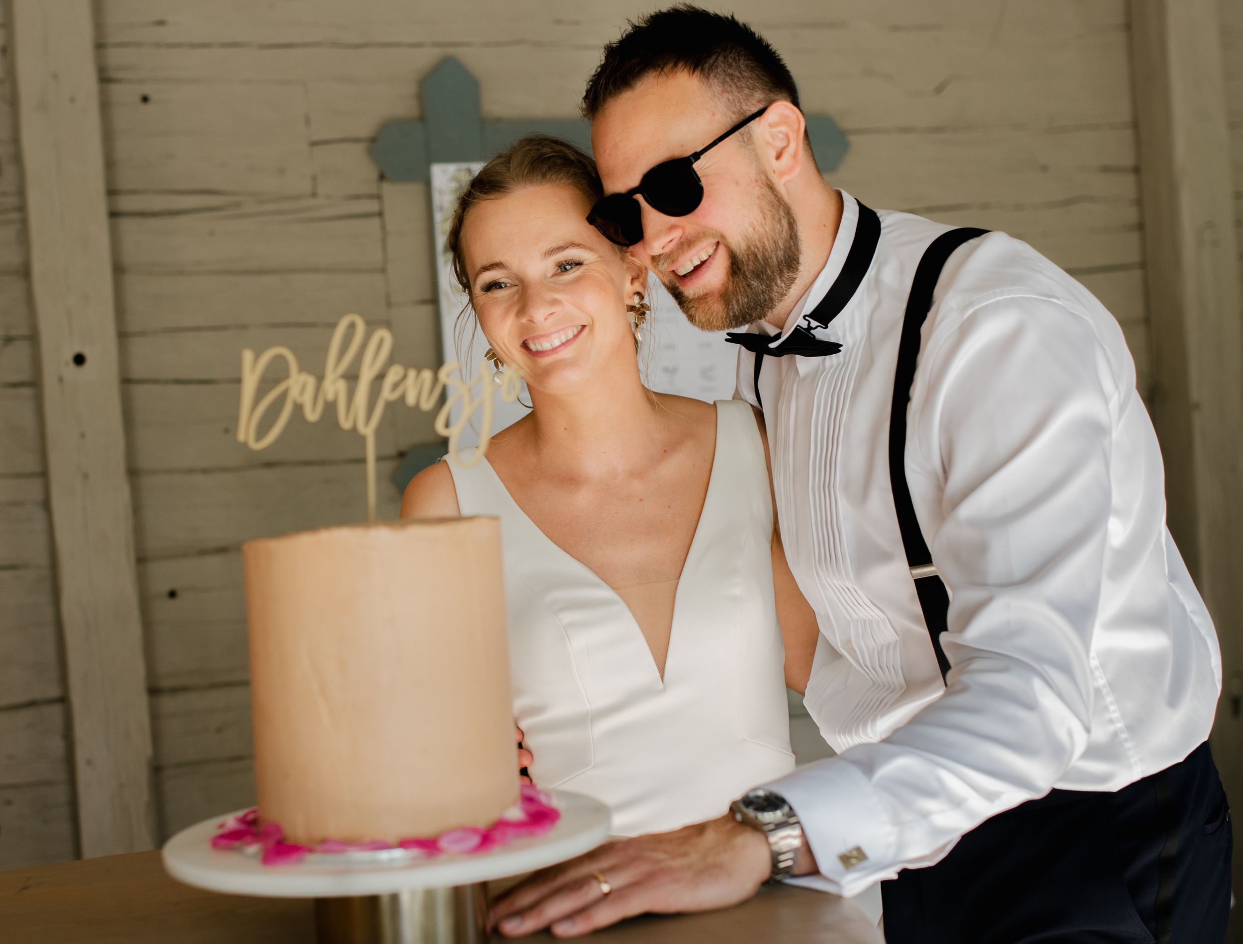 Wedding couple standing next to a pink-accented cake.