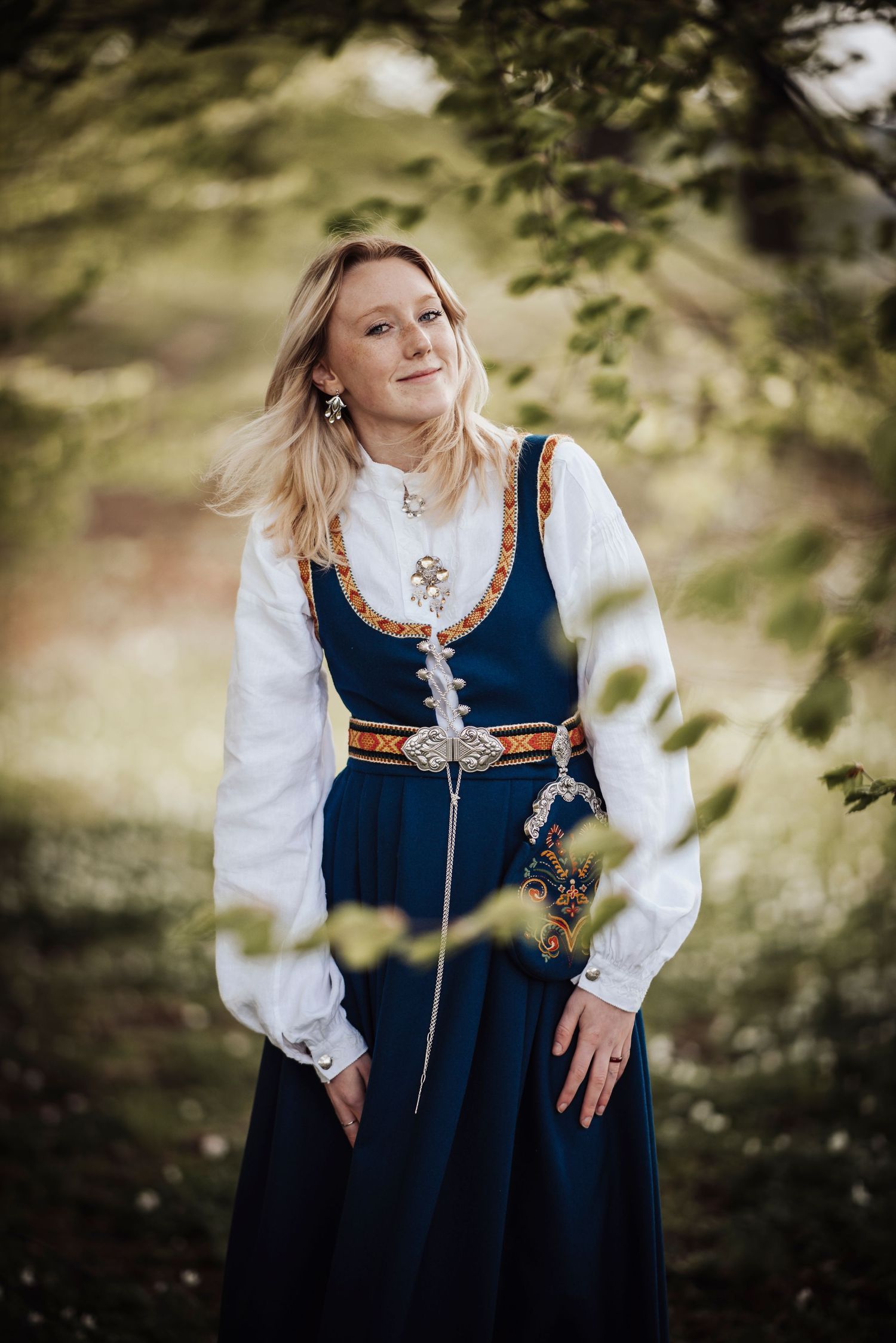 Traditional Scandinavian dress with navy bodice, white sleeves and ornate trim photographed in natural outdoor setting.