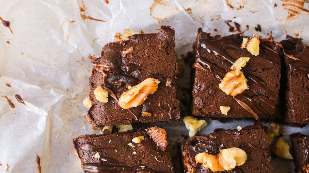 Rich chocolate brownies topped with nuts and caramel on parchment paper.