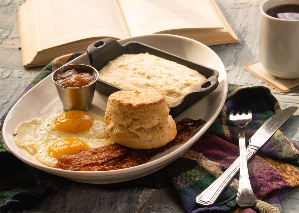 Breakfast plate with biscuits, eggs, bacon and syrup alongside an open book.