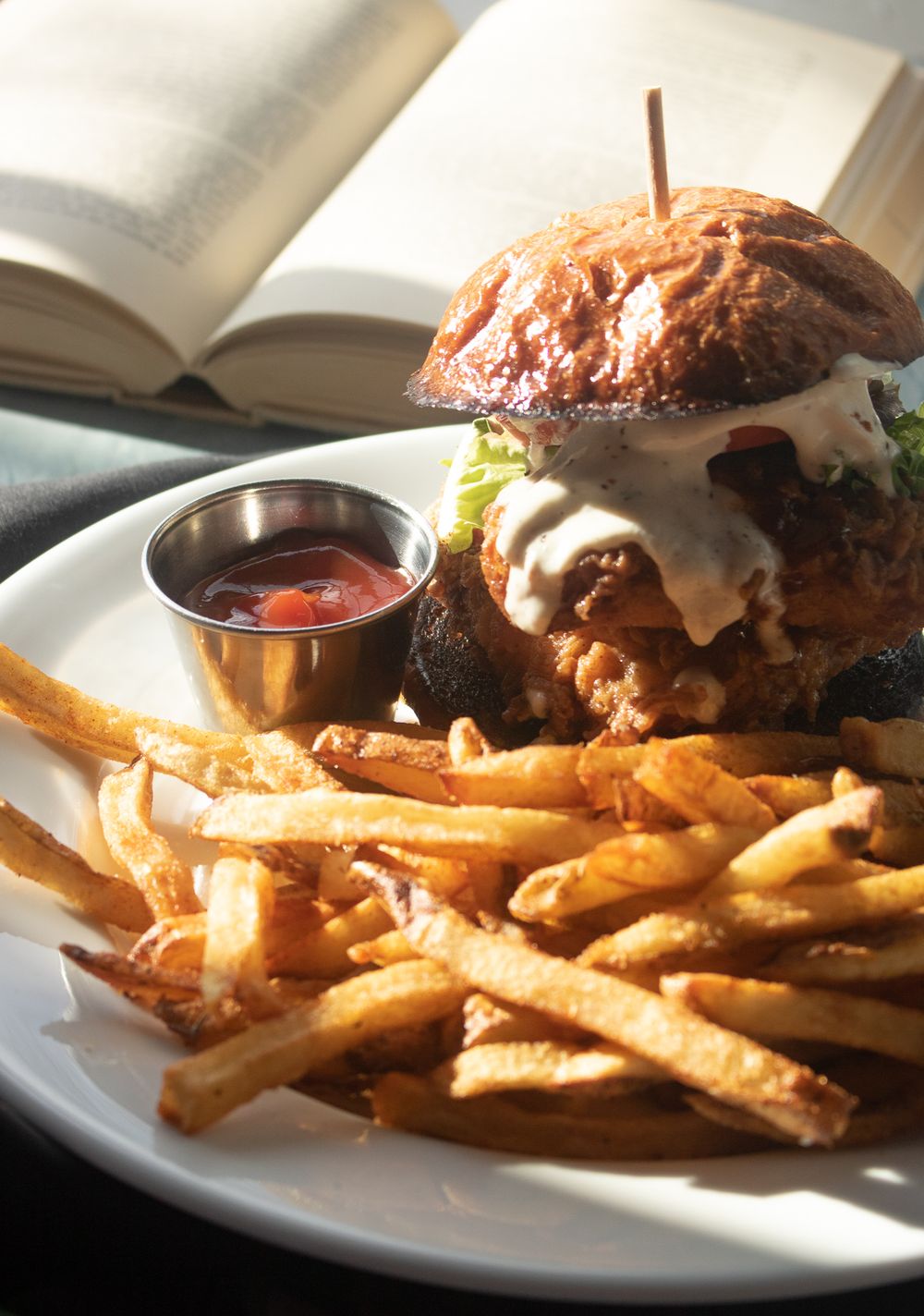 Juicy burger with melted cheese and crispy french fries served with dipping sauce next to an open book.