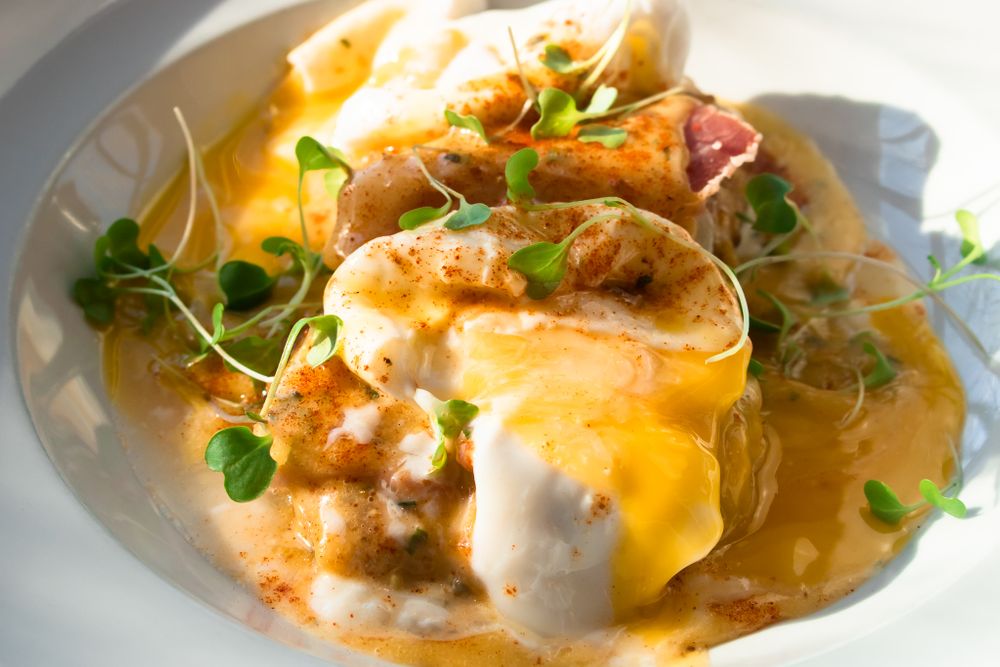 Eggs Benedict with hollandaise sauce and microgreens on white plates.