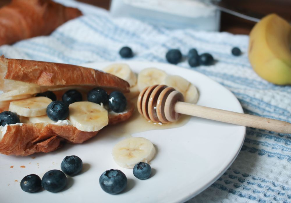 Fresh blueberries, banana slices and honey drizzler arranged on a white plate.