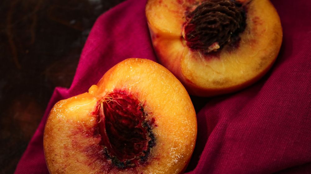 Fresh ripe peaches with dark centers arranged on a burgundy background.