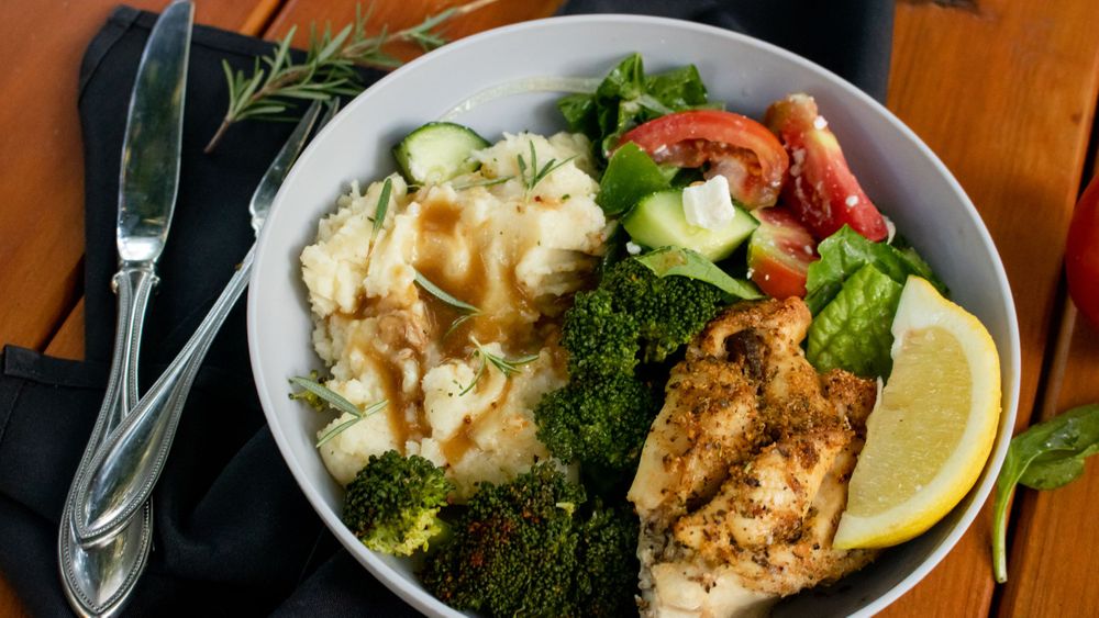 Grilled chicken breast with steamed broccoli, tomatoes and lemon garnish served on white plates.