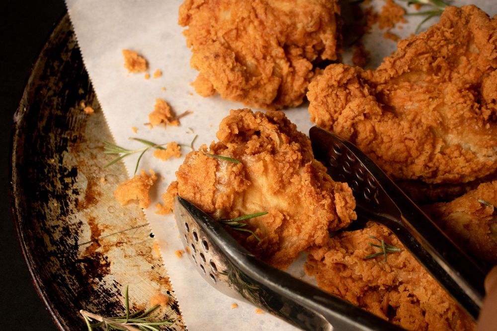 Crispy fried chicken pieces being served with metal tongs.
