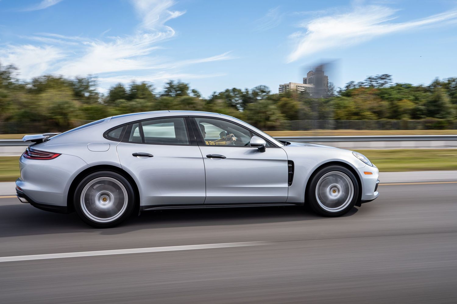 Silver Porsche Panamera luxury sedan driving on highway with motion blur effect.