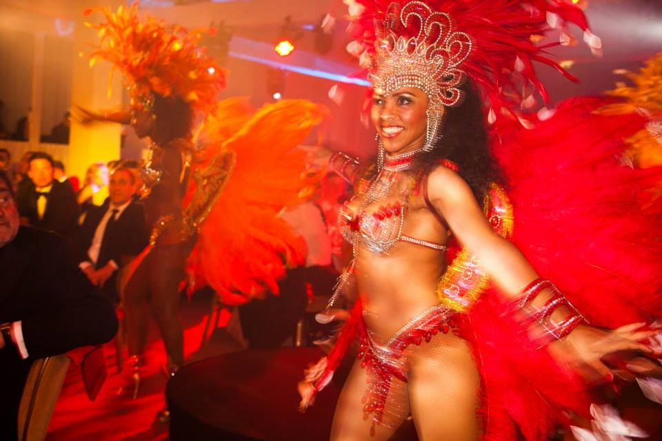 Brazilian carnival dancer in red feathered costume performs at a vibrant event.
