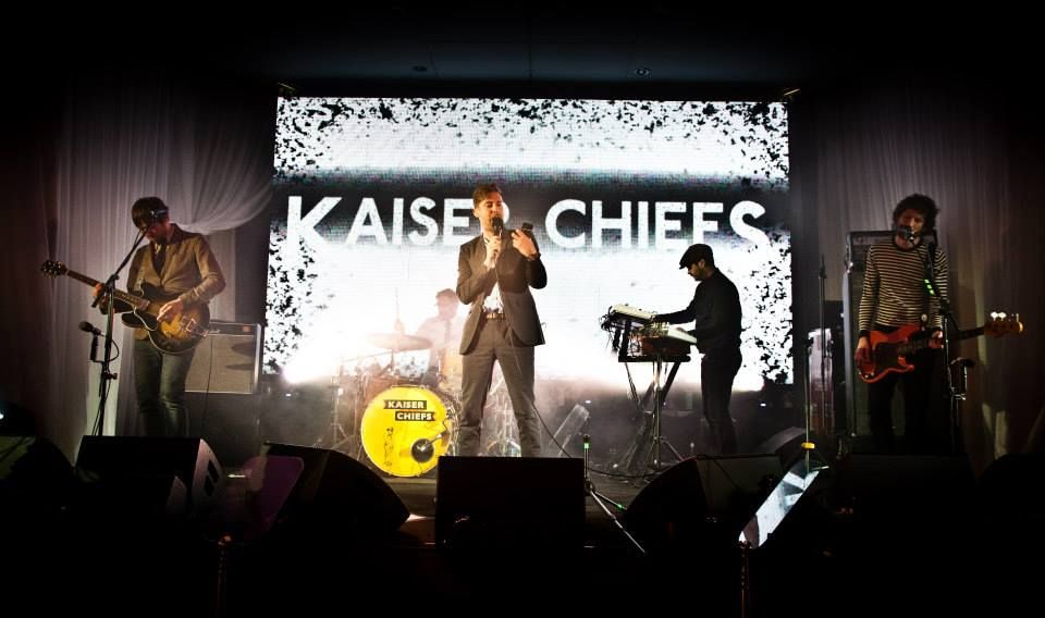 Kaiser Chiefs perform live on stage with dramatic backlighting and band name display.