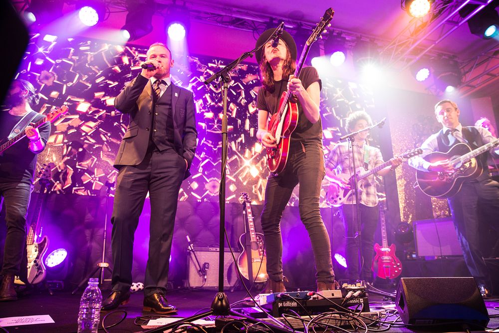 Band performing on stage with dramatic purple lighting and decorative backdrop.