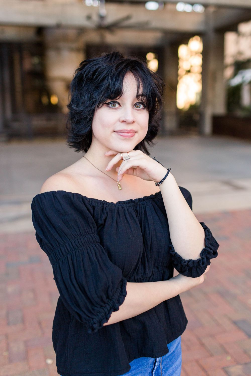 A person in a black off-shoulder top poses against an urban backdrop.