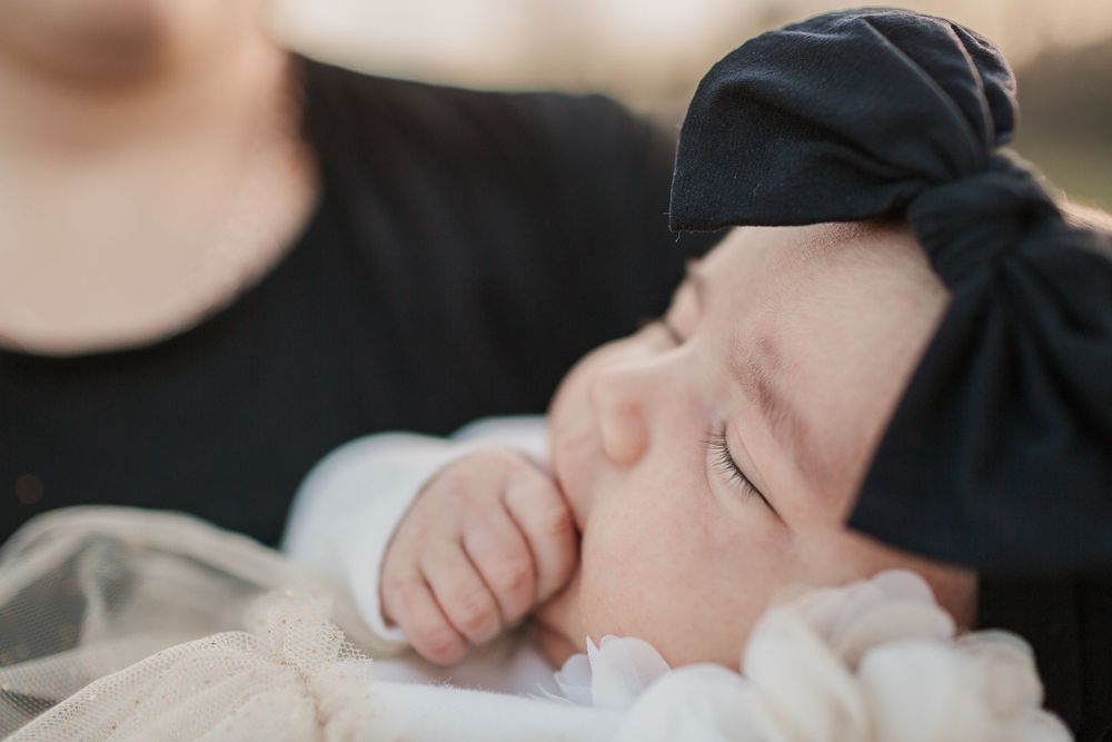 Sleeping baby wearing a black bow headband in soft natural light.