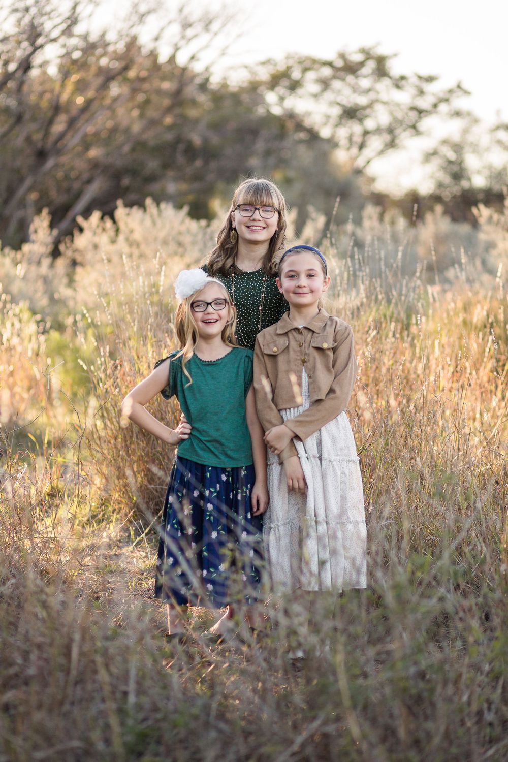 Three siblings in coordinating outfits posing together in golden autumn grass.