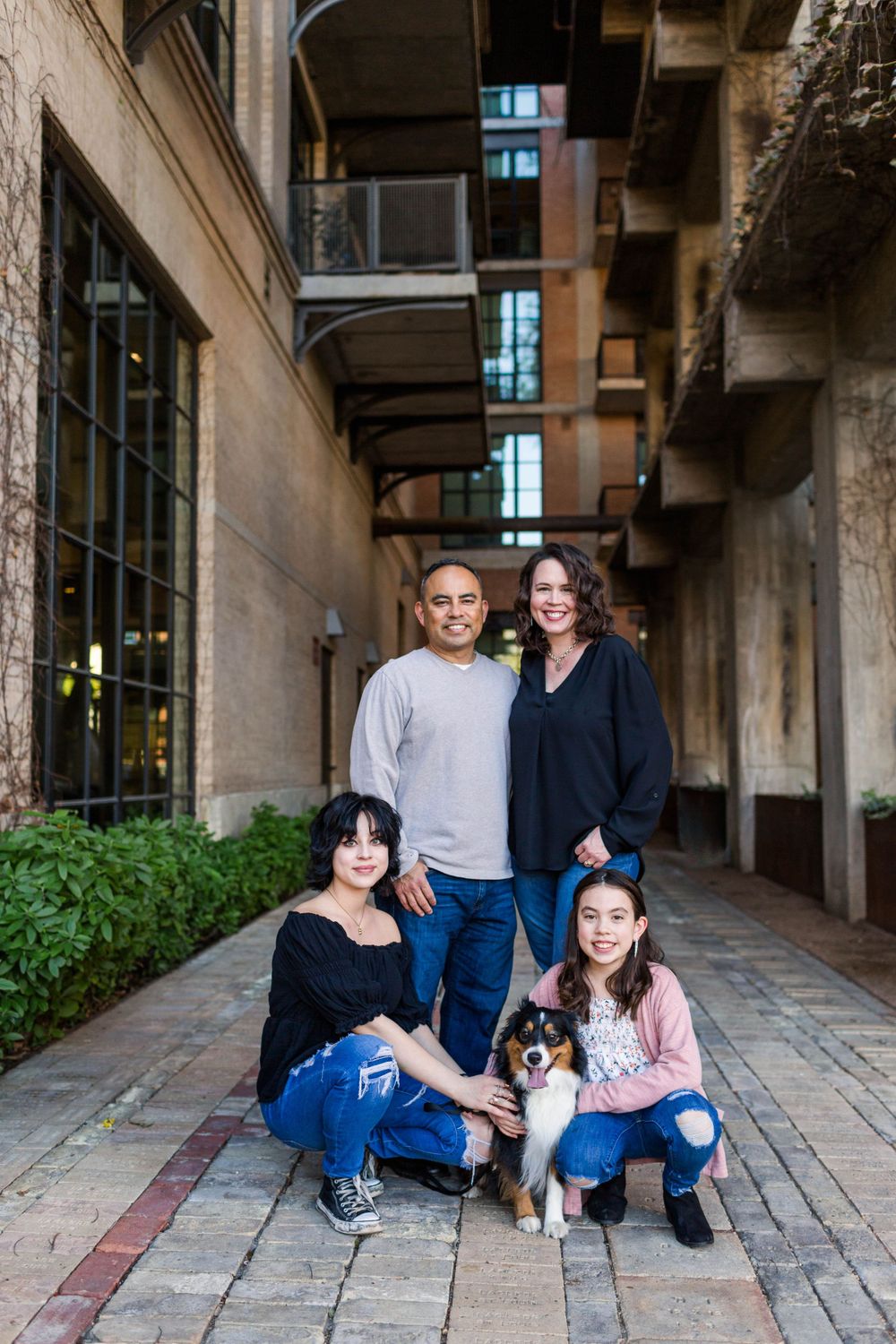 A group of friends and their dog pose together in an urban courtyard setting.