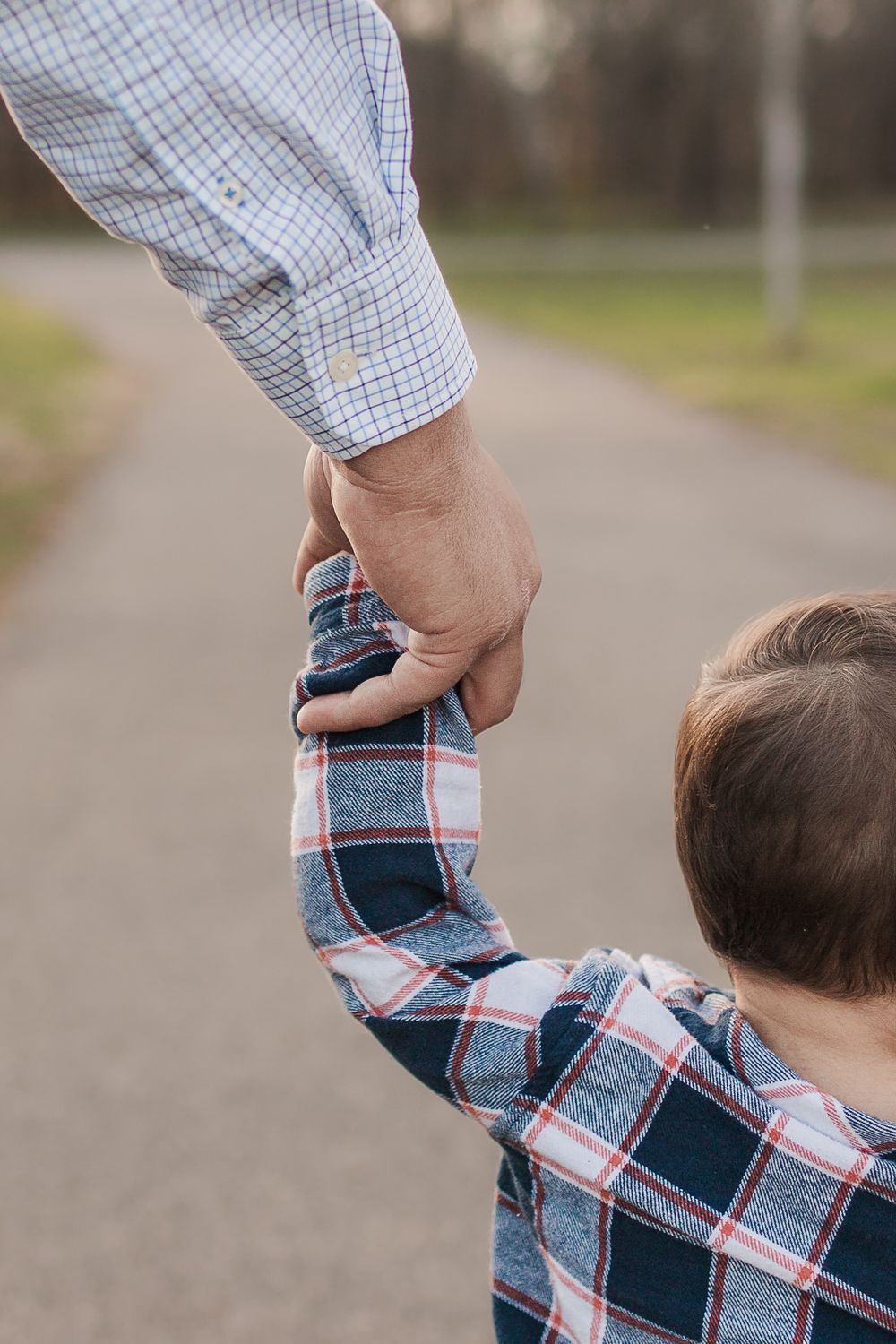 Close-up of parent holding child's hand while walking on a path.